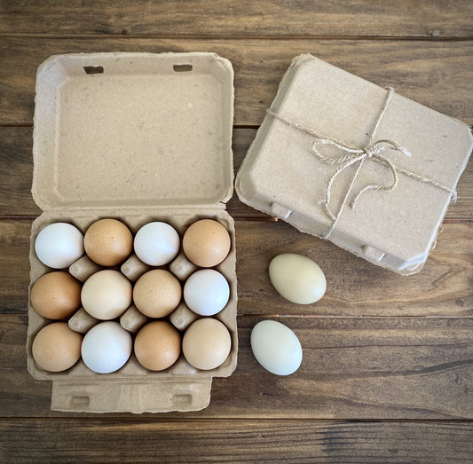 A My Pet Chicken Henlay Vintage Blank Egg Carton (classic 3x4 design, available in 2 colors and multiple pack sizes) holds fresh eggs on a wooden table beside two loose eggs and a closed carton made from recycled cardboard.