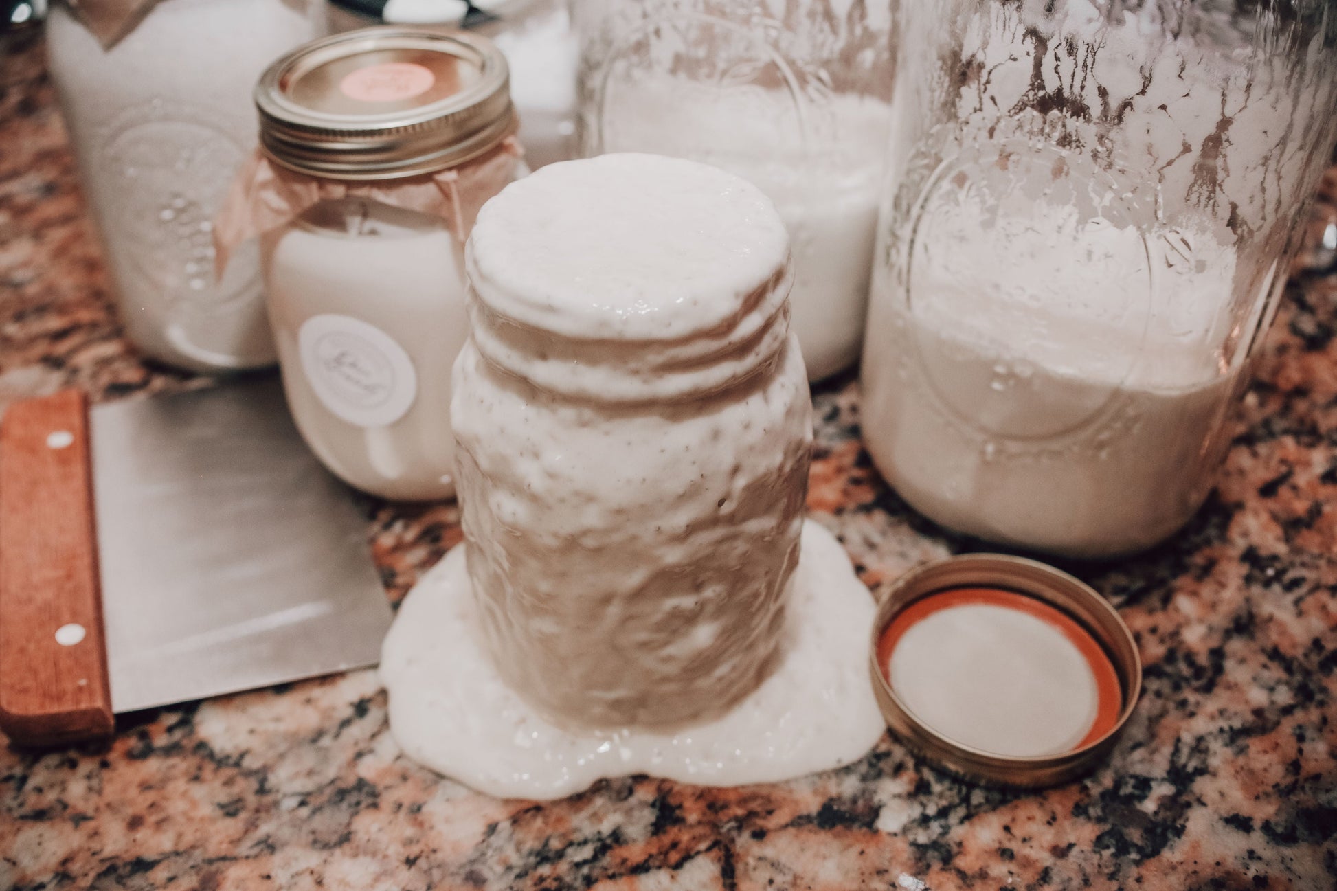 Onic Brands LLC sourdough starter jar with a clear label and a wooden spoon on a rustic wooden surface.