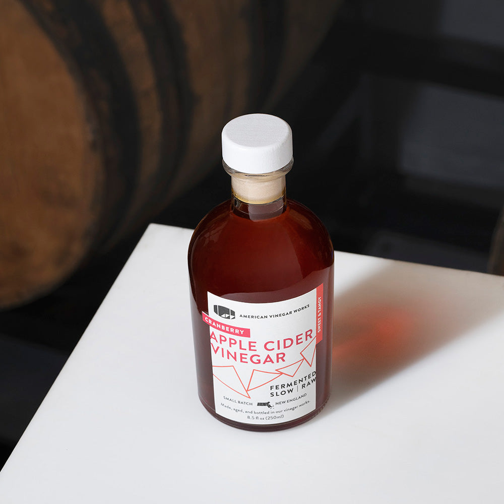 Bottle of American Vinegar Works cranberry apple cider vinegar showing the label and clear glass bottle on a white background.