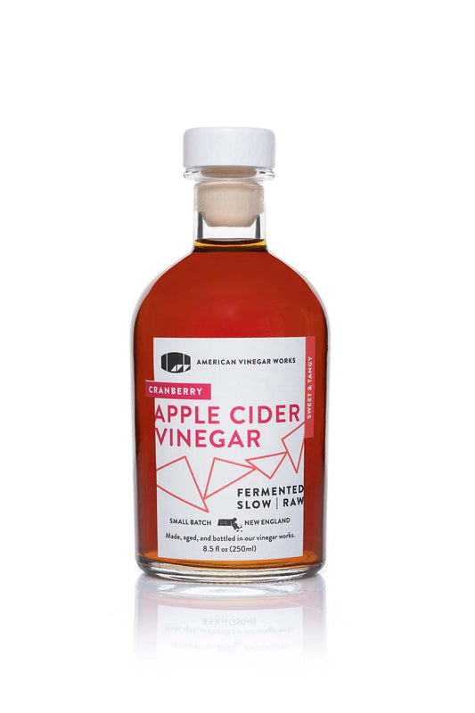 American Vinegar Works cranberry apple cider vinegar bottle with a label featuring cranberries and apples, clear glass bottle.
