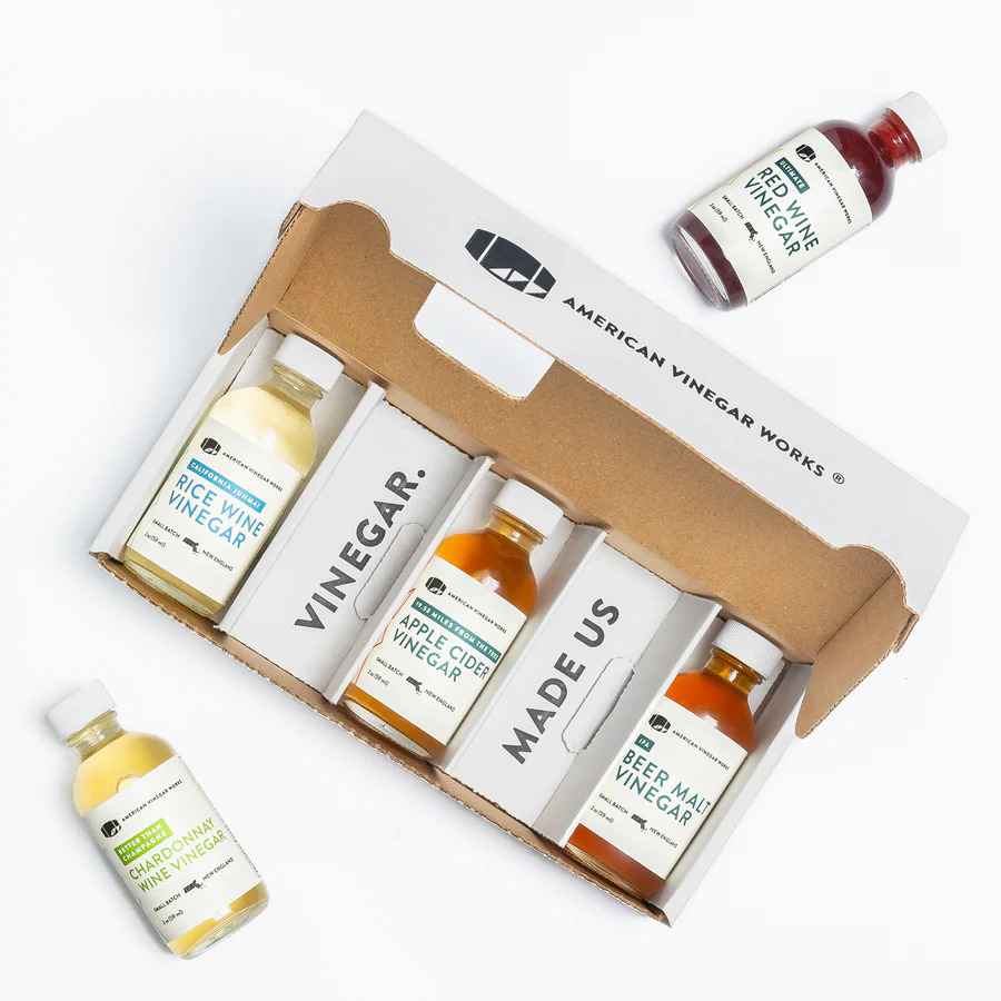 American Vinegar Works Essentials Plus vinegar sampler pack featuring small bottles of various craft vinegars on a white background.