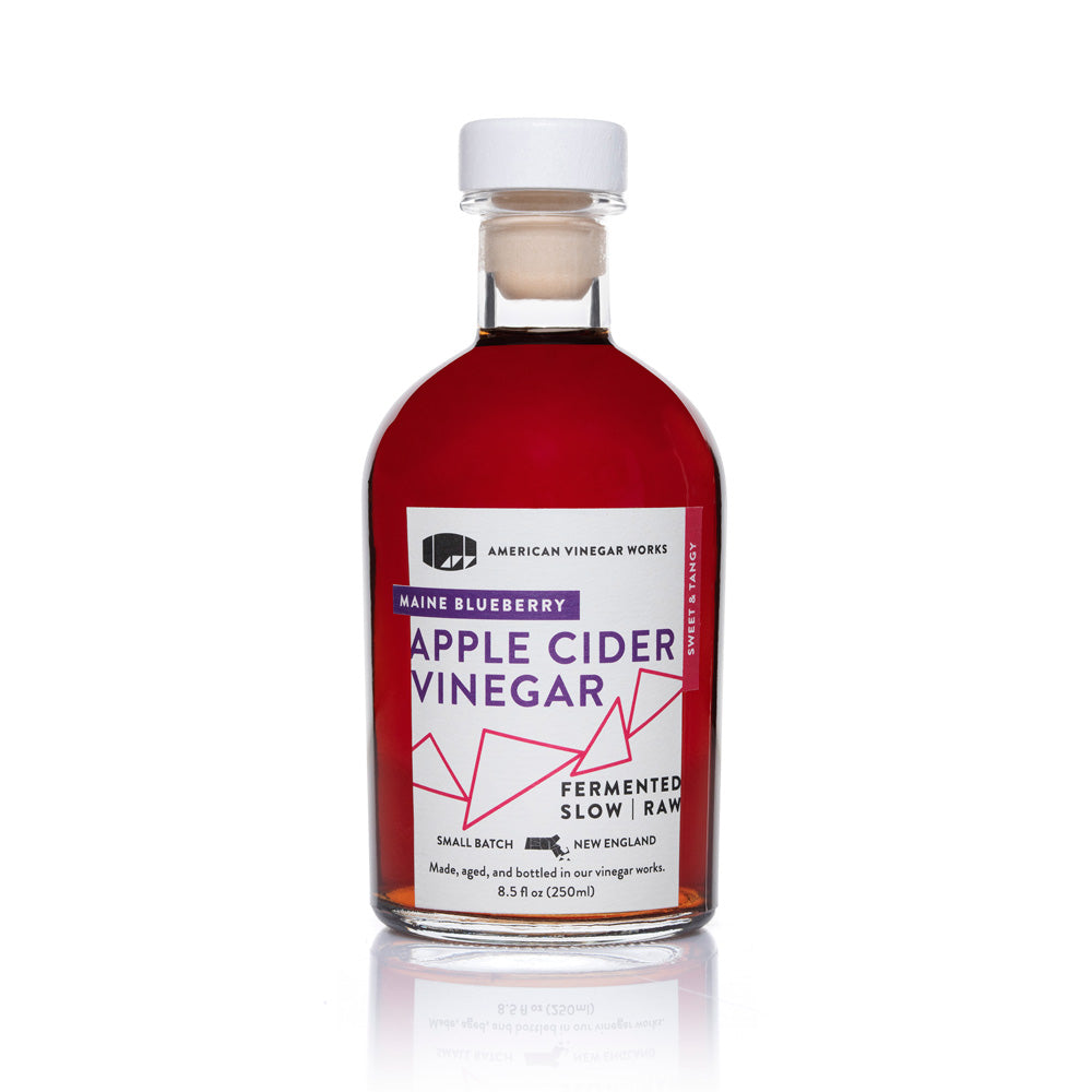 Front view of American Vinegar Works wild blueberry apple cider vinegar bottle, showcasing its label and dark amber liquid inside.