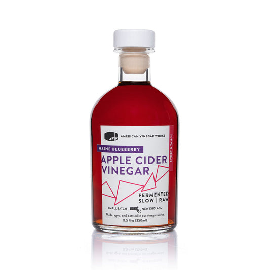 Front view of American Vinegar Works wild blueberry apple cider vinegar bottle, showcasing its label and dark amber liquid inside.