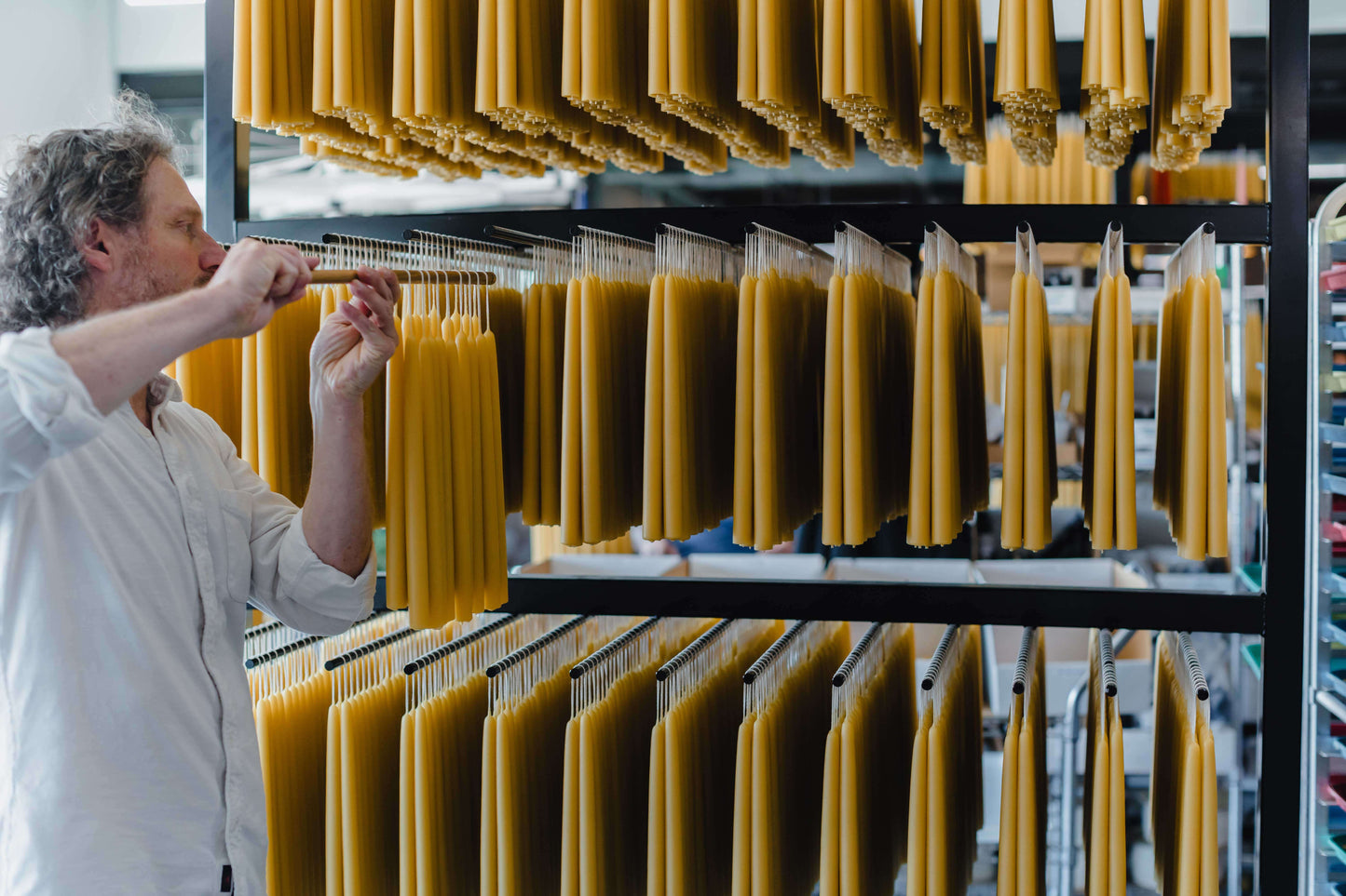 Bluecorn Candles hand-dipped beeswax taper candles in a bundle, with founder Jon Kornbluh placing the candles on a rack.
