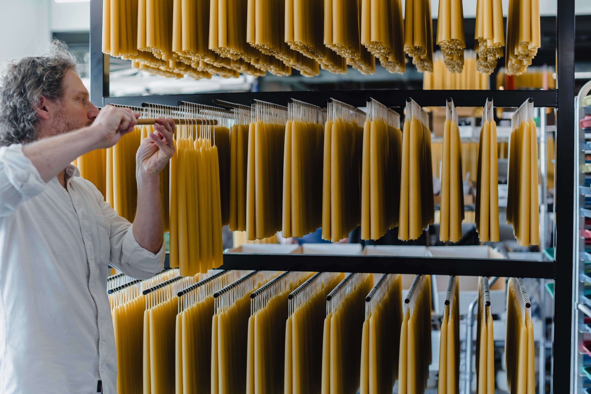 Bluecorn Candles hand-dipped beeswax taper candles in a bundle, with founder Jon Kornbluh placing the candles on a rack.