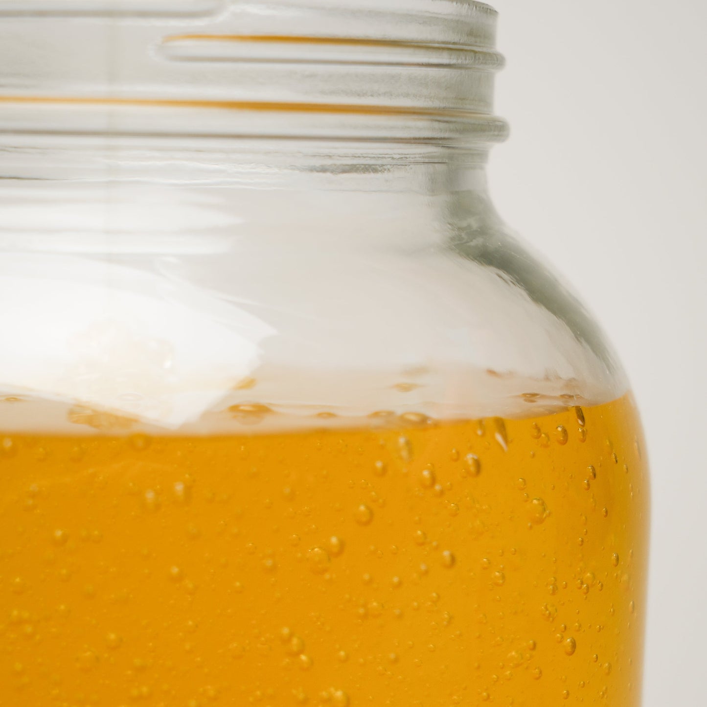 Close-up of a glass jar filled with golden honey-like liquid, evoking the natural purity of Rustic Strengths Castile Soap - Ultra Concentrate | Unscented, set partially visible against a plain, light background.