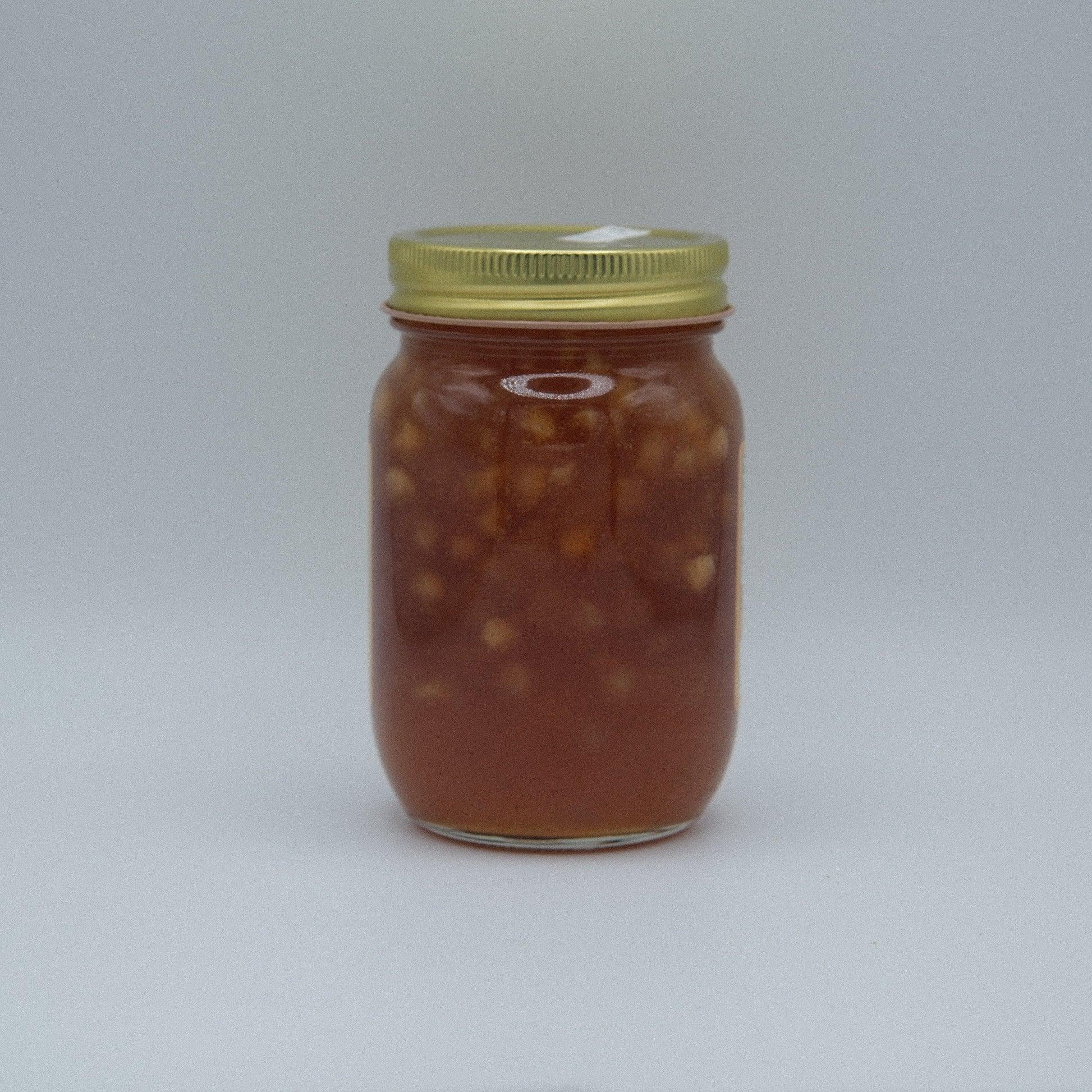 Canned Apple Pie Jam by Amish Country Store in a jar, showcasing glossy apple and spice filling with a golden hue.