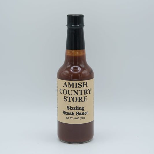 Bottle of Amish Country Store sizzling steak sauce showing rich, savory sauce in a glass bottle with a red label and white cap.