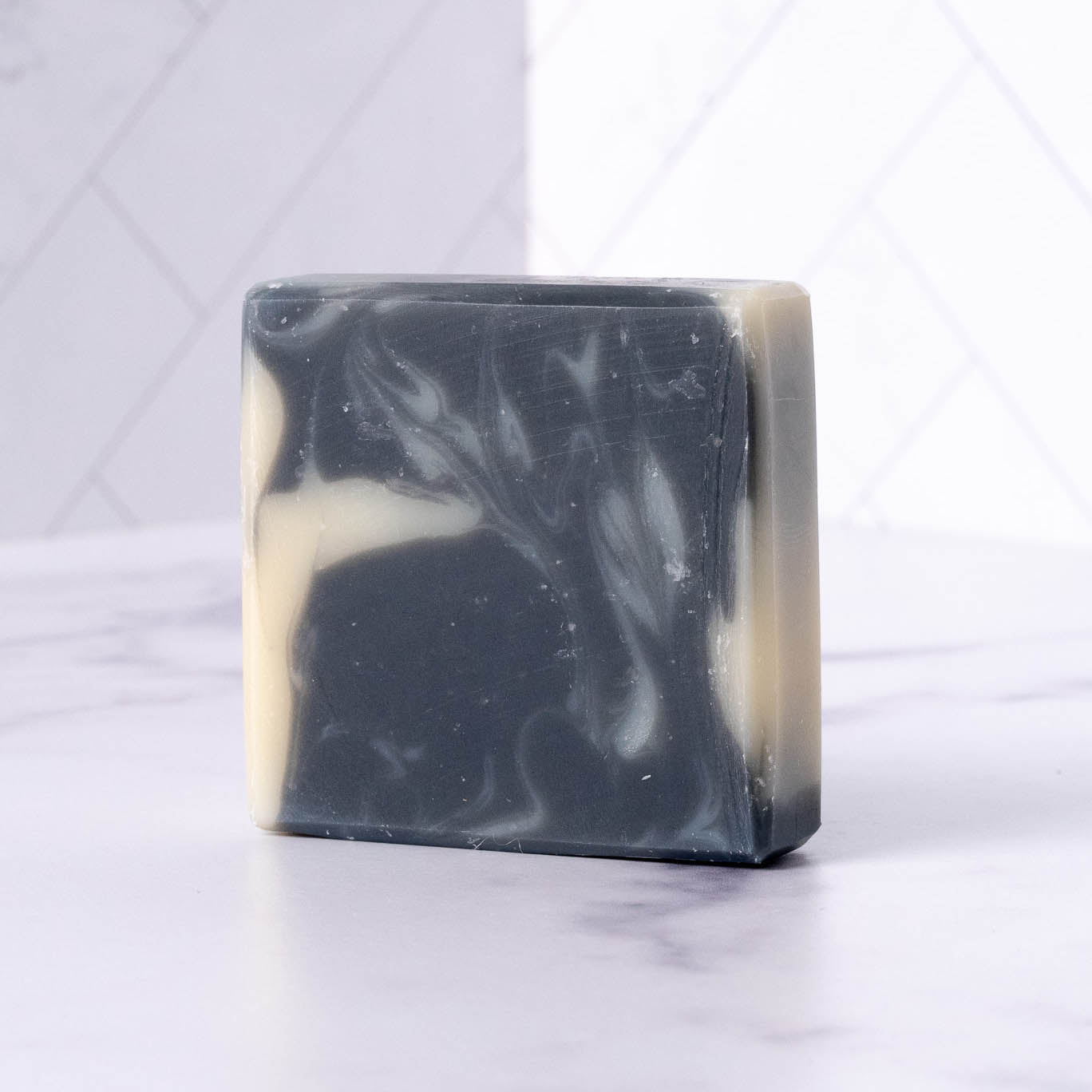 Rustic Strength Bar Soap | Detoxifying Charcoal, a rectangular marbled black and white soap for sensitive skin, rests on white marble with a light tiled wall in the background.