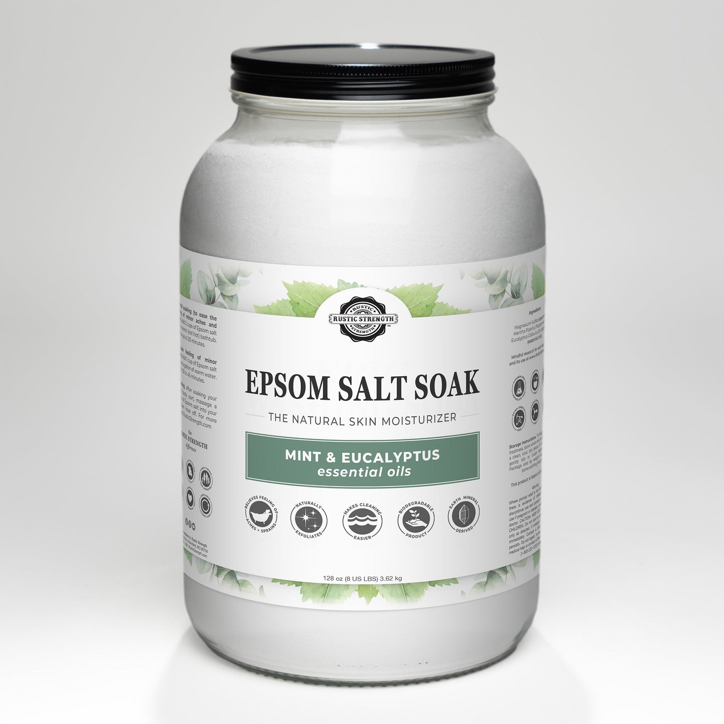 A large clear jar with a black lid, Rustic Strength’s Epsom Salt Soak | Mint & Eucalyptus features green leaves on the label and pure essential oils for a refreshing scent. Described as a natural skin moisturizer.