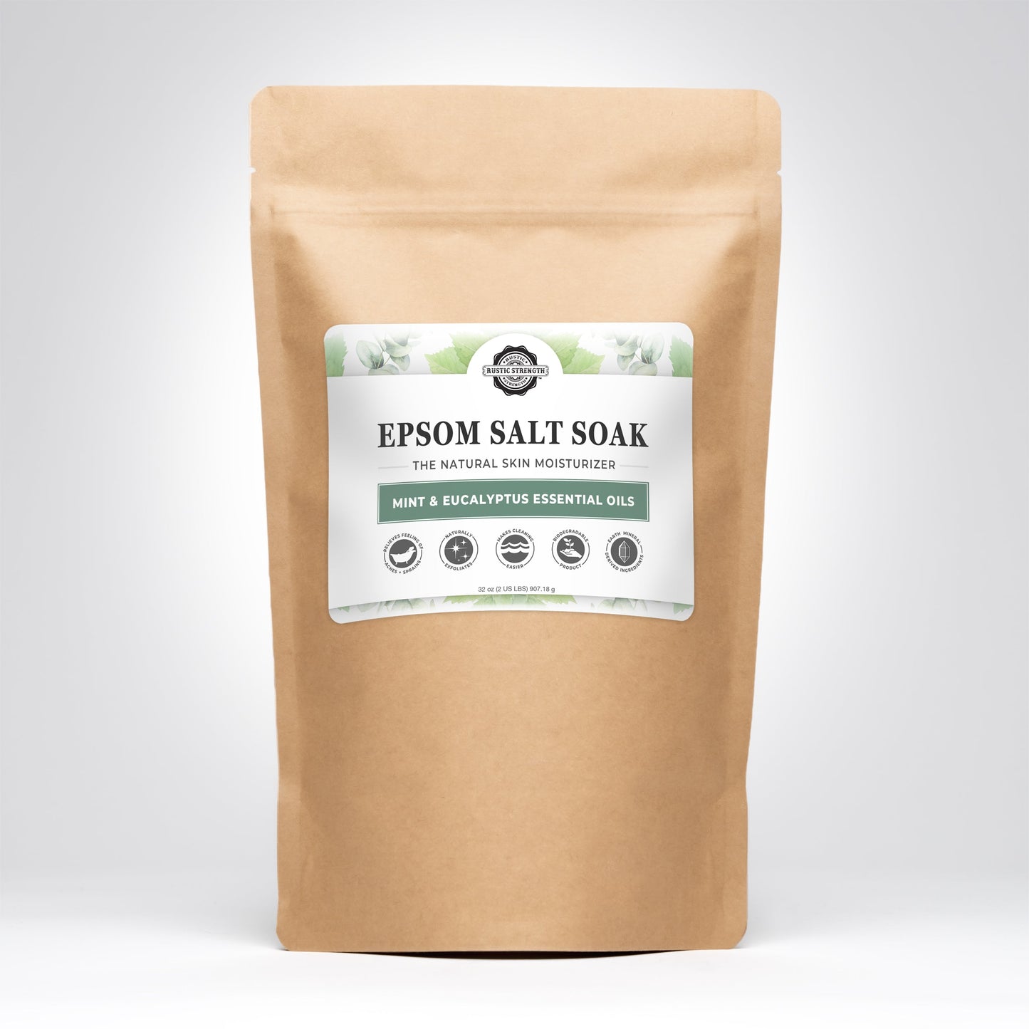 A brown resealable pouch labeled Rustic Strength Epsom Salt Soak | Mint & Eucalyptus stands upright on a white background. The label features green leaf accents, product info, and notes its grey-water safe formula.