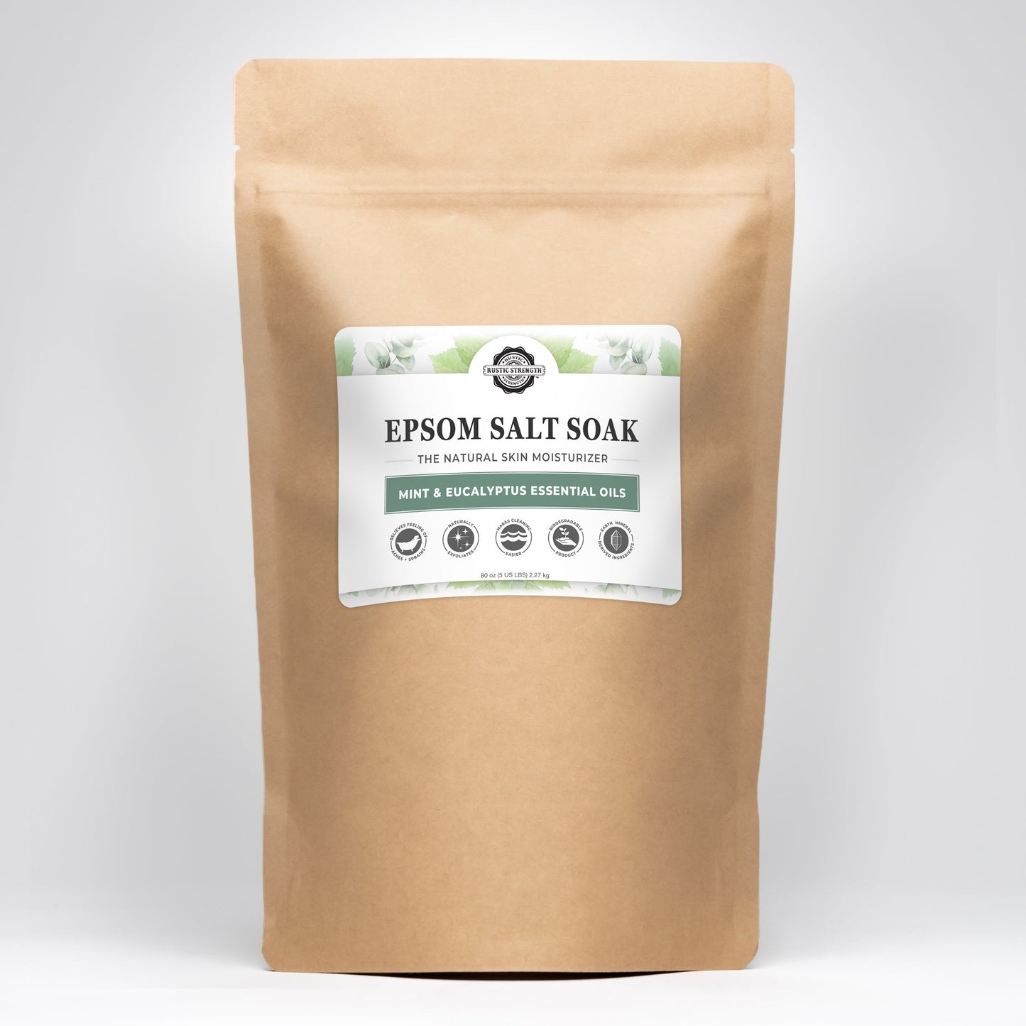 A brown resealable bag labeled “Epsom Salt Soak | Mint & Eucalyptus” by Rustic Strength, scented with pure essential oils, displays icons for natural, vegan, cruelty-free, recyclable, and grey-water safe on a plain light background.