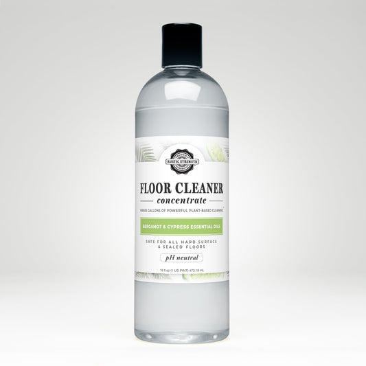 Rustic Strength Floor Cleaner Concentrate | Bergamot & Cypress comes in a clear plastic bottle with a black cap and white label with green leaves. Its plant-based, pH neutral, non-toxic, and infused with bergamot & cypress essential oils.