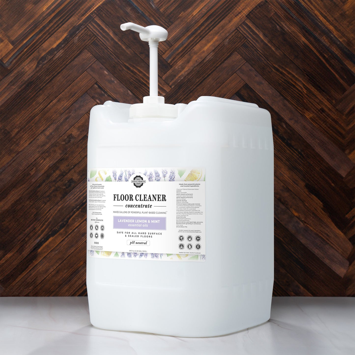 A large white pump bottle labeled Rustic Strength Floor Cleaner Concentrate | Lavender, Lemon & Mint, with lavender graphics and plant-based formula details, sits on a wooden floor.