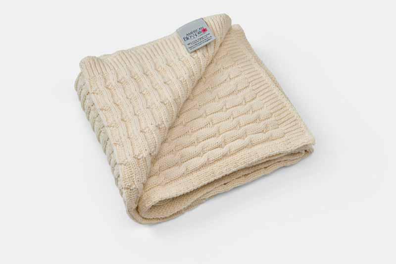 Folded American Blossom Linens cotton knitted baby blanket with label, showcasing soft, cozy 100% cotton fabric for infants.