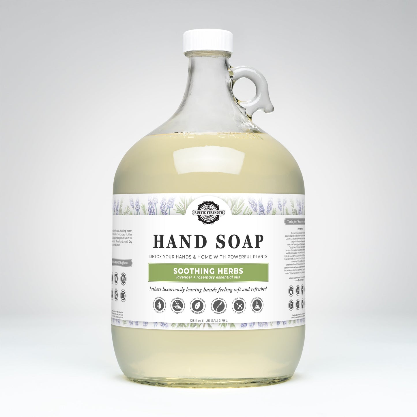 A large clear bottle of Rustic Strength Hand Soap | Soothing Herbs with a handle, featuring lavender and herb illustrations on the label, highlights gentle, biodegradable cleansing and natural ingredients.