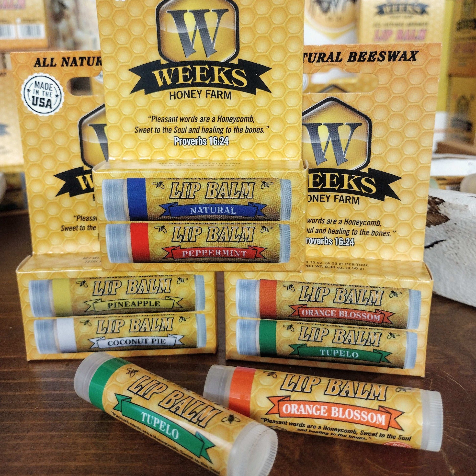 Weeks Honey Farm All Natural Beeswax Lip Balms are available as singles, twin packs, or by the case—featuring flavors such as peppermint and coconut pie—displayed before yellow honeycomb boxes for soft, protected lips.