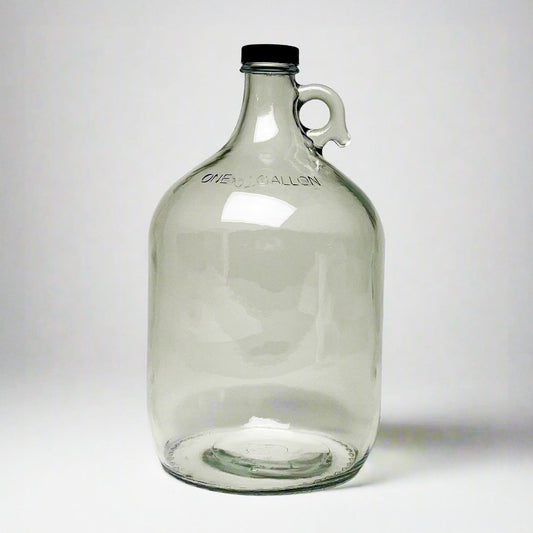 The Rustic Strength 1 Gallon Glass Jug with Cap features a clear glass body, black screw cap, small side handle, and ONE GALLON embossing near the top. Limited stock available.