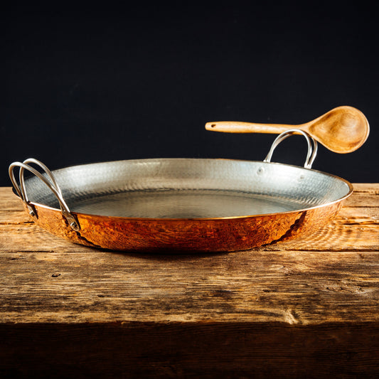 Alicante Copper Paella Pan by Sertodo with a wooden spoon, showcasing the large, round copper cookware for traditional paella preparation.