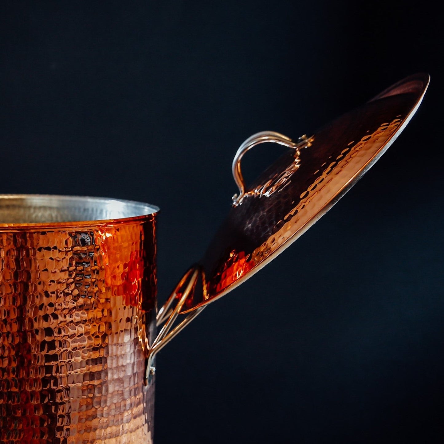 Close-up of Sertodo copper stock pot lid resting on the handle, showcasing the shiny, durable copper finish and detailed craftsmanship.