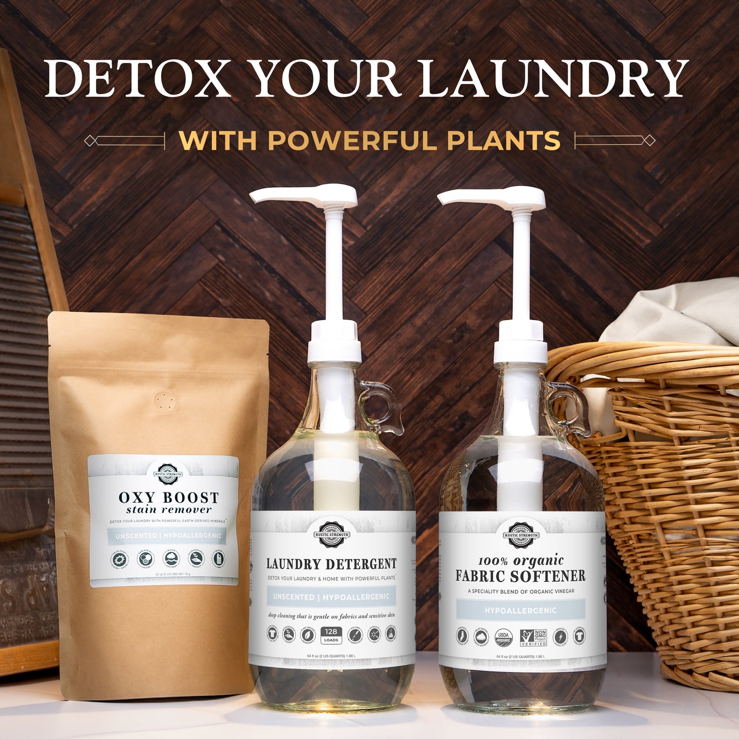 A laundry setup features Rustic Strength’s Mama + Baby Safe Laundry Detergent in a pump bottle, 100% Organic Fabric Softener, and an Oxy Boost Stain Remover brown pouch, all arranged on a wooden surface with a wicker basket.