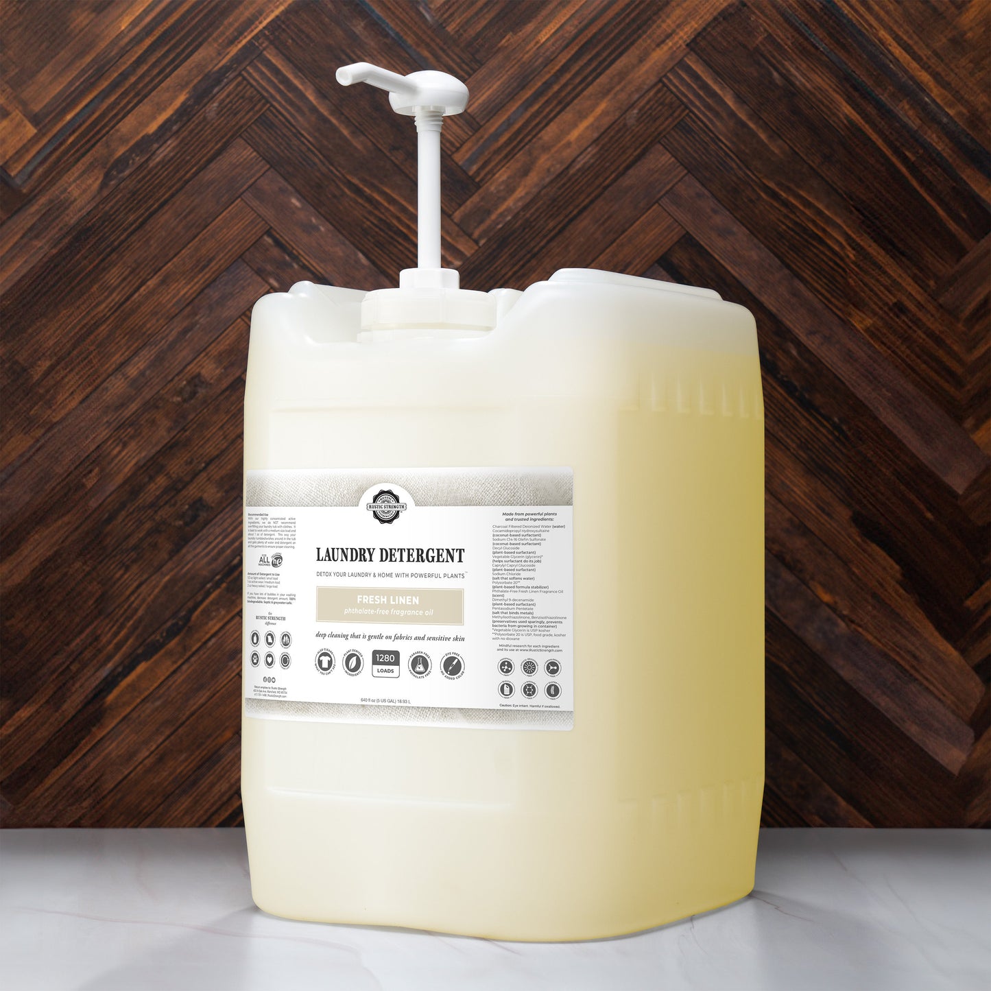A large translucent pump bottle of Rustic Strength Laundry Detergent | Fresh Linen, filled with yellow hypoallergenic liquid, sits on a wooden surface before a herringbone-patterned wood wall.