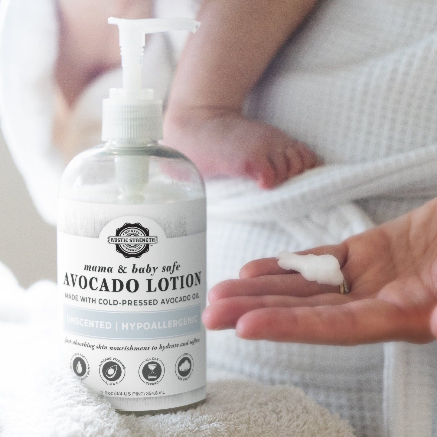 A person dispenses Rustic Strength Avocado Lotion | Mama + Baby Safe onto their hand while holding a baby in a white towel; this lotion gently hydrates with nourishing avocado oil.