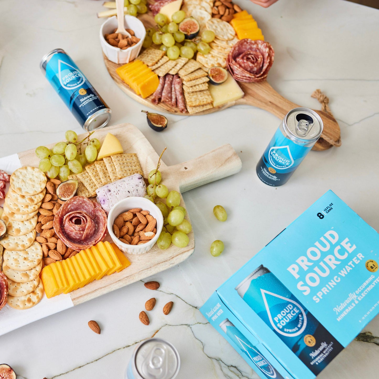 Cans of PROUD SOURCE WATER alkaline spring water, displayed in a lifestyle setting with clear labels and sleek design.