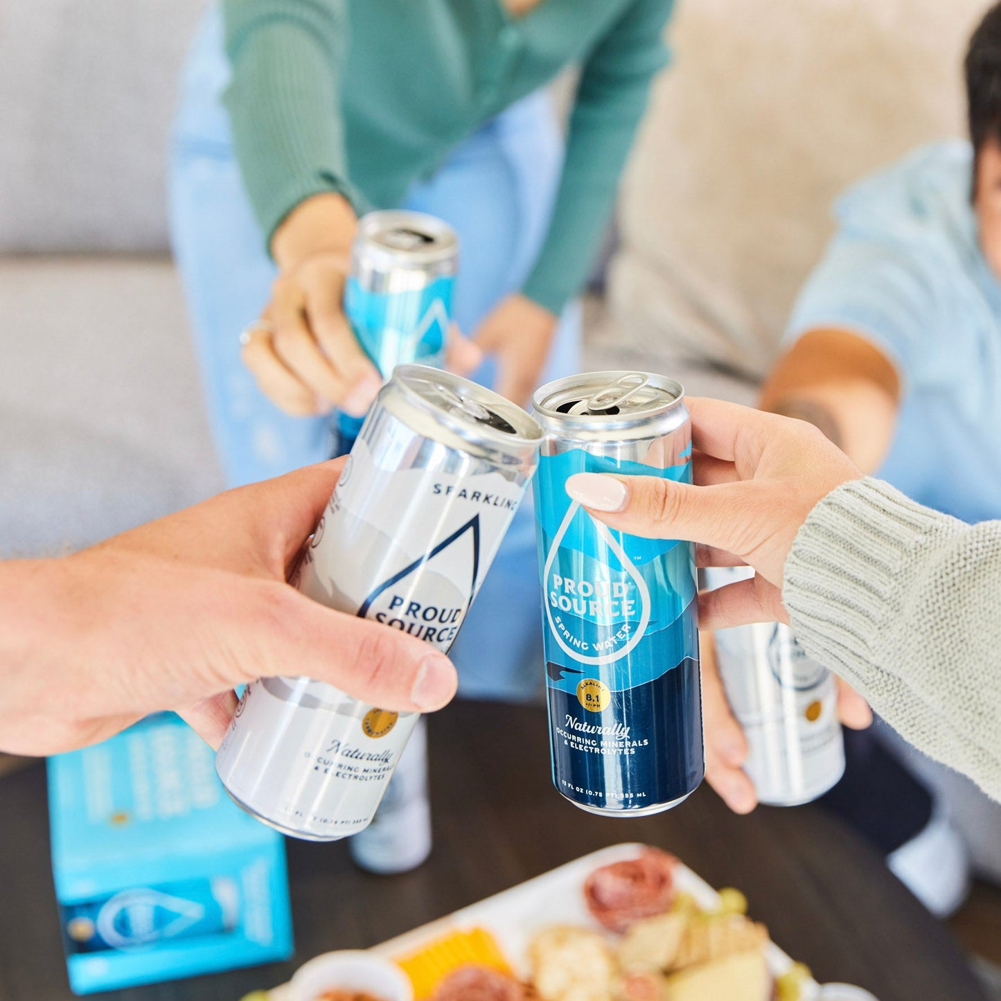 Three sparkling spring water cans from PROUD SOURCE WATER on a table, showcasing their sleek design and refreshing appearance.