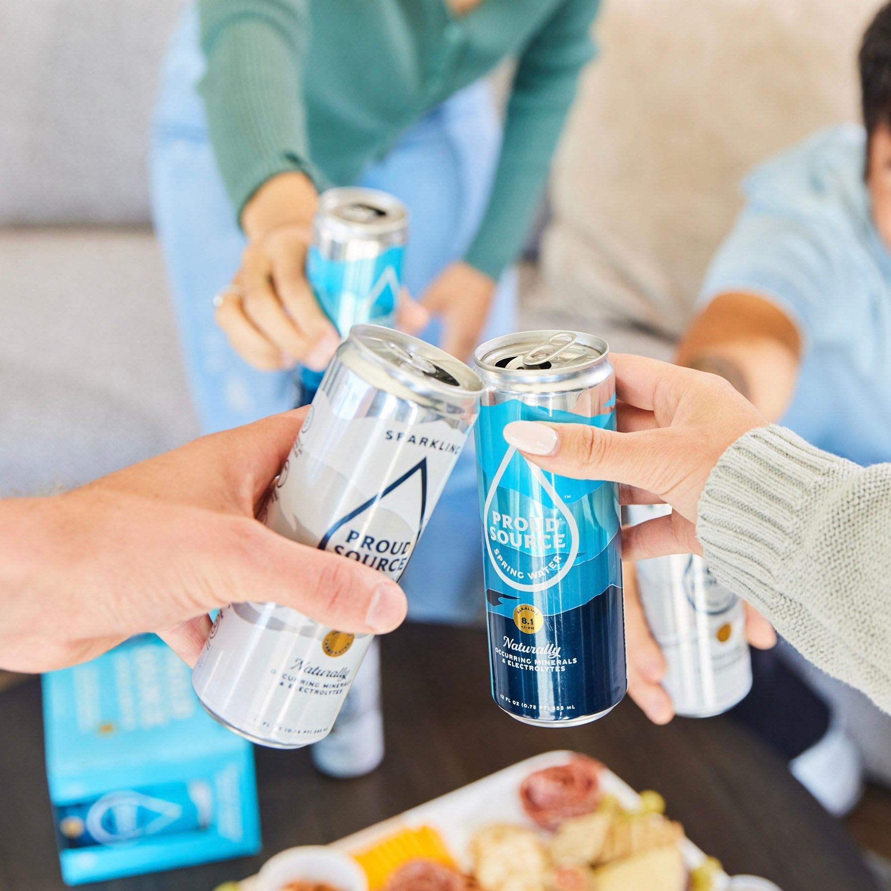 Three sparkling spring water cans from PROUD SOURCE WATER on a table, showcasing their sleek design and refreshing appearance.
