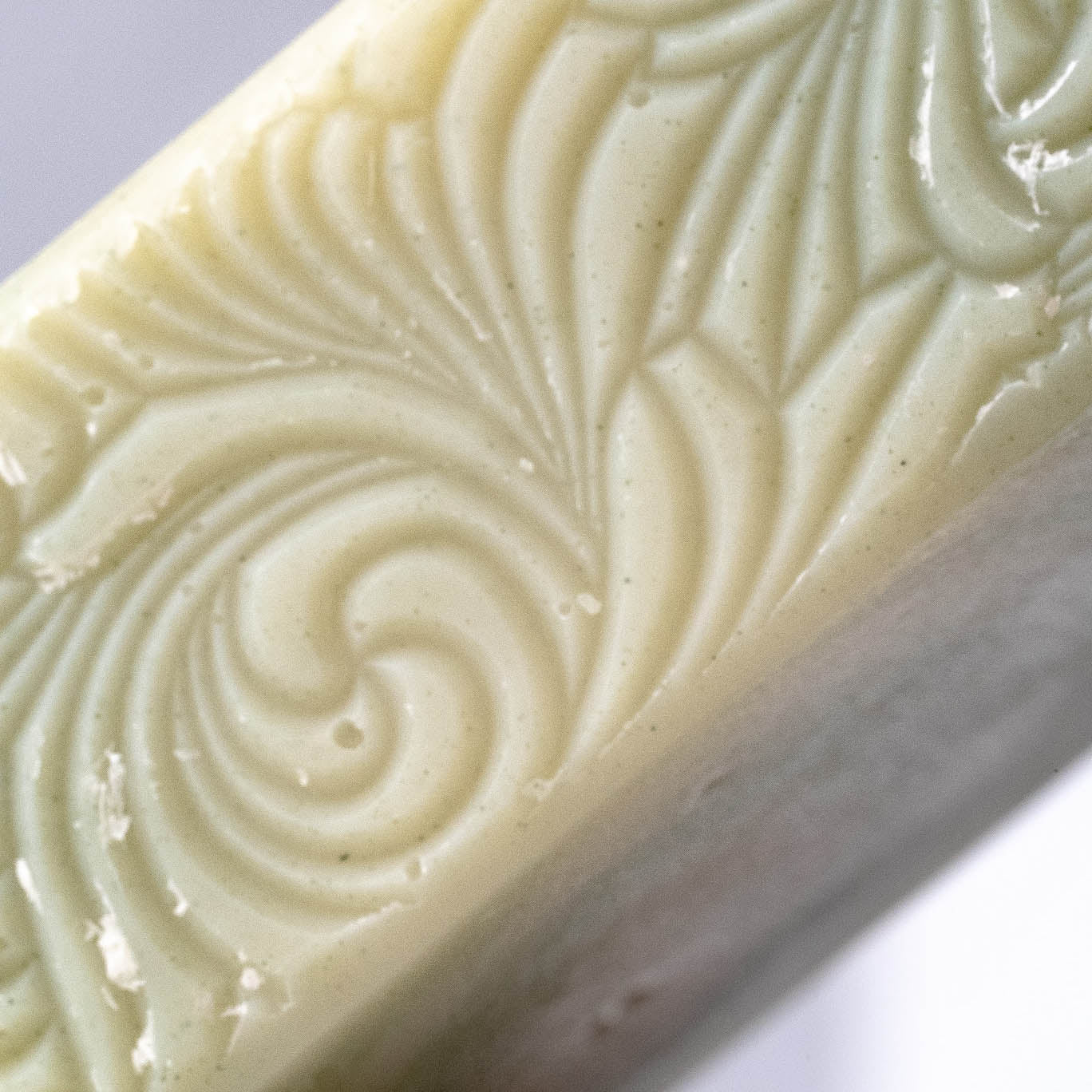 A close-up of Rustic Strengths Bar Soap | Peppermint Tea Tree showcases its pale, creamy surface adorned with intricate, swirling embossed patterns.