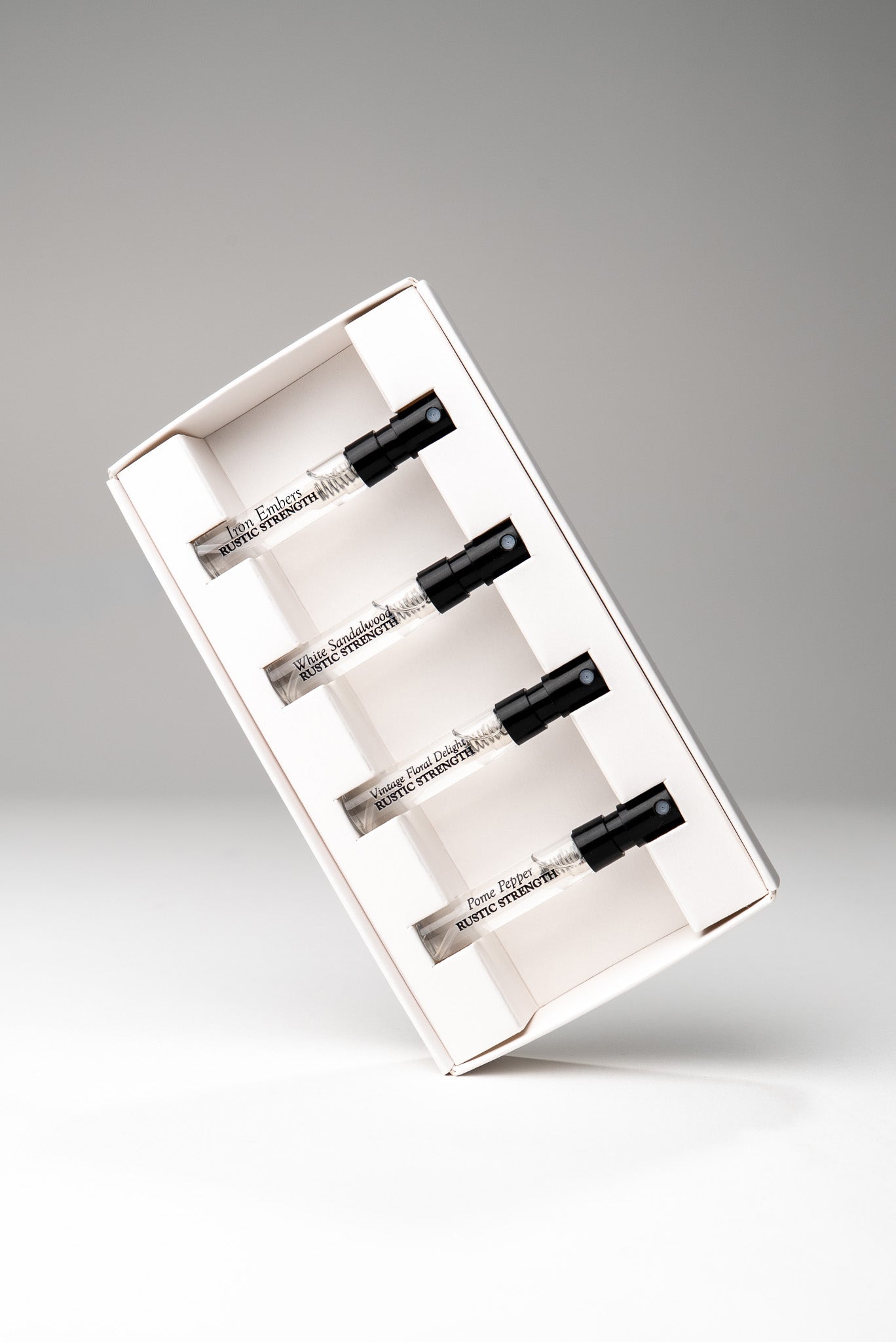 Set of six Rustic Strength perfume scent samples in small glass vials with white caps, arranged in a transparent plastic tray.