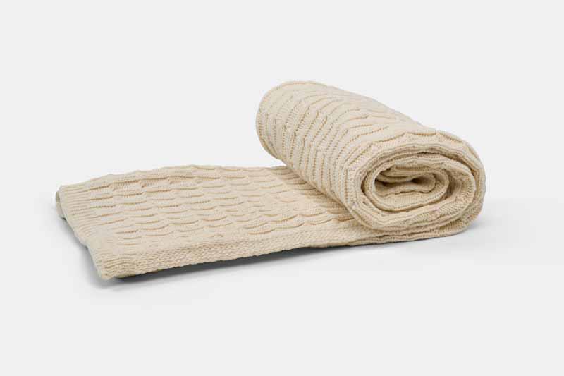 Cream-colored cotton knitted baby blanket from American Blossom Linens, rolled to show soft, textured knit fabric.