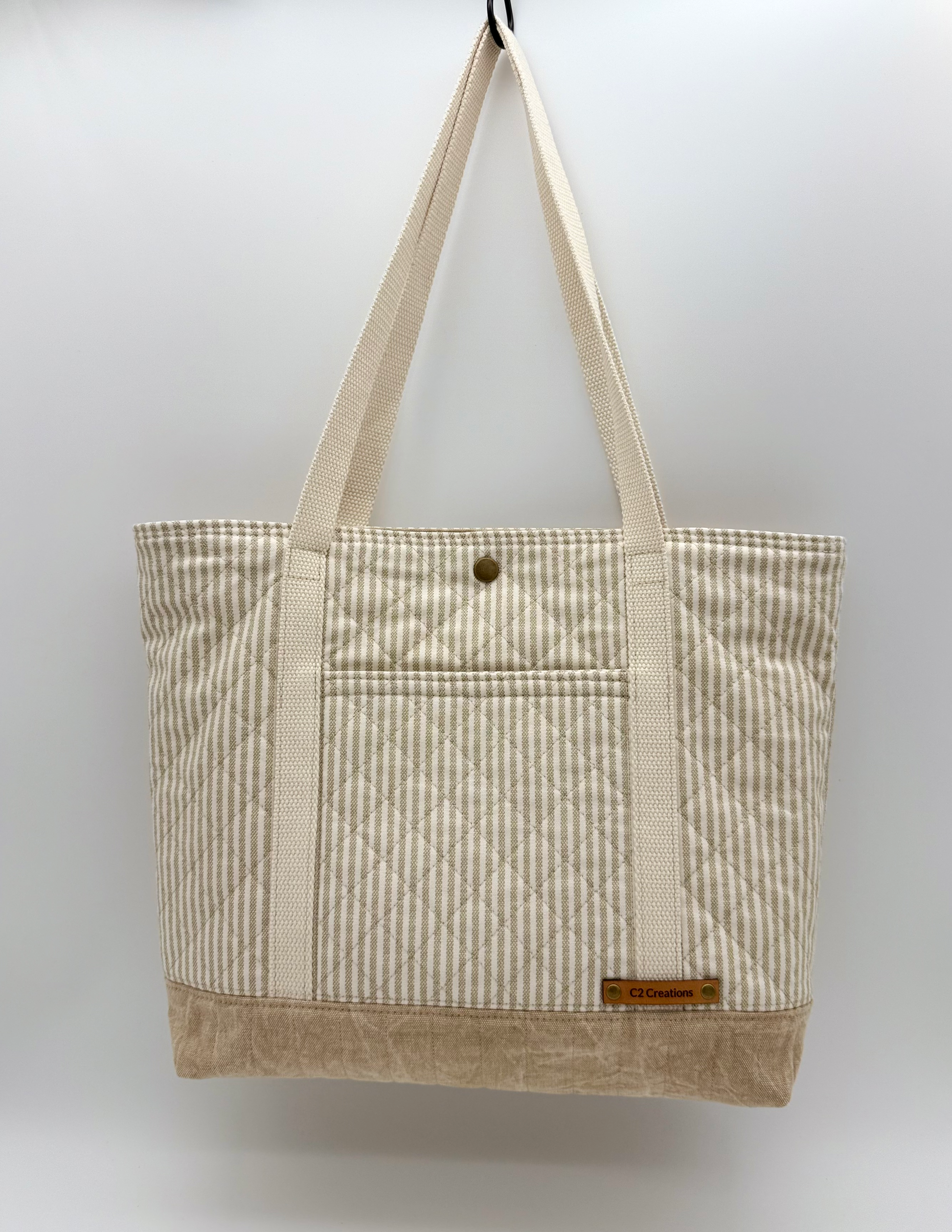Taupe striped quilted canvas tote bag with snap closure, handmade by C2 Creations LLC, front view showing quilted pattern and tote handles.
