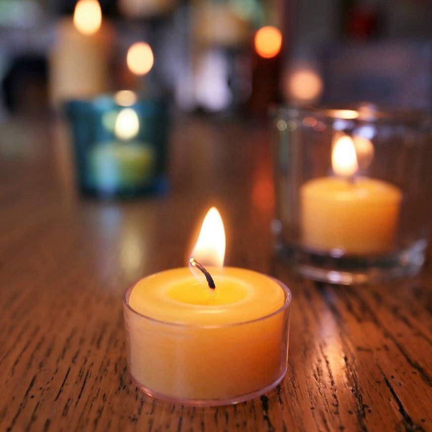 Bluecorn Candles pure beeswax tea light candles in a clear container, showcasing their warm, natural honey color and smooth surface.