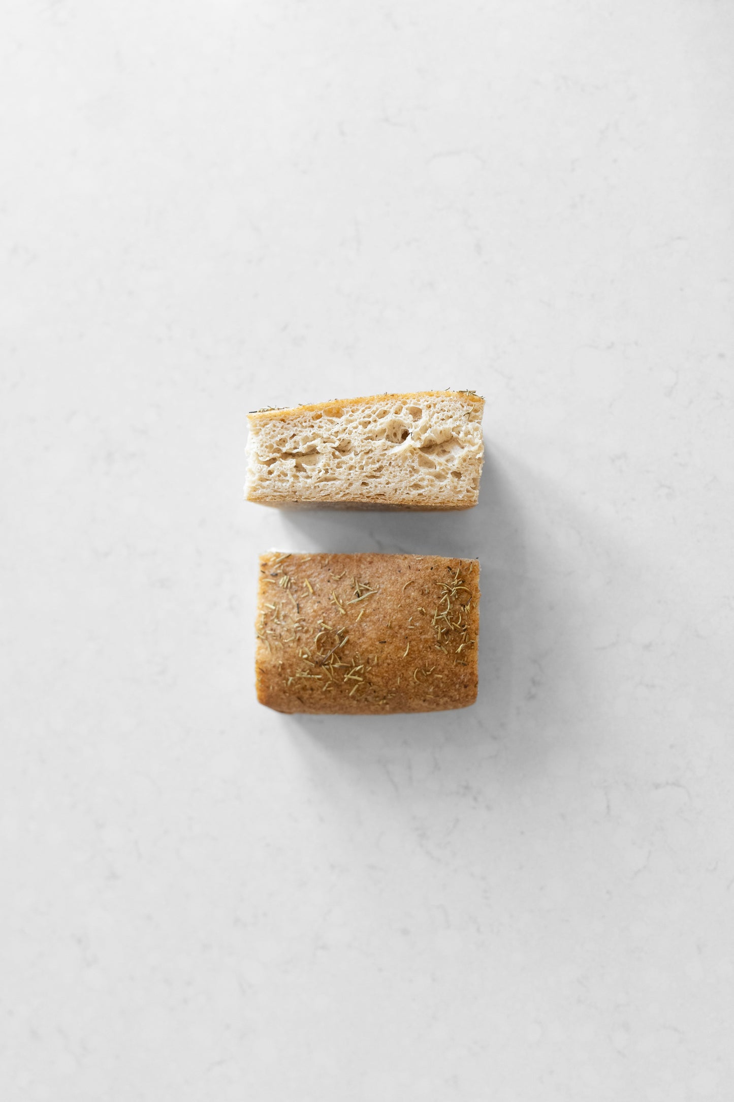 Two slices of gluten-free rosemary focaccia sourdough bread from Heaven Gluten Free Bakery, showing golden crust and rosemary topping.