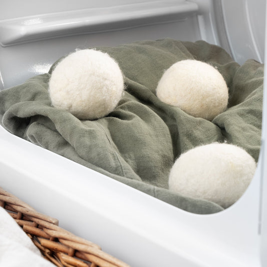 Three Rustic Strength Jumbo Wool Dryer Balls (3 pack) made from sheep wool rest on green fabric inside a dryer, with part of a wicker basket visible in the foreground.