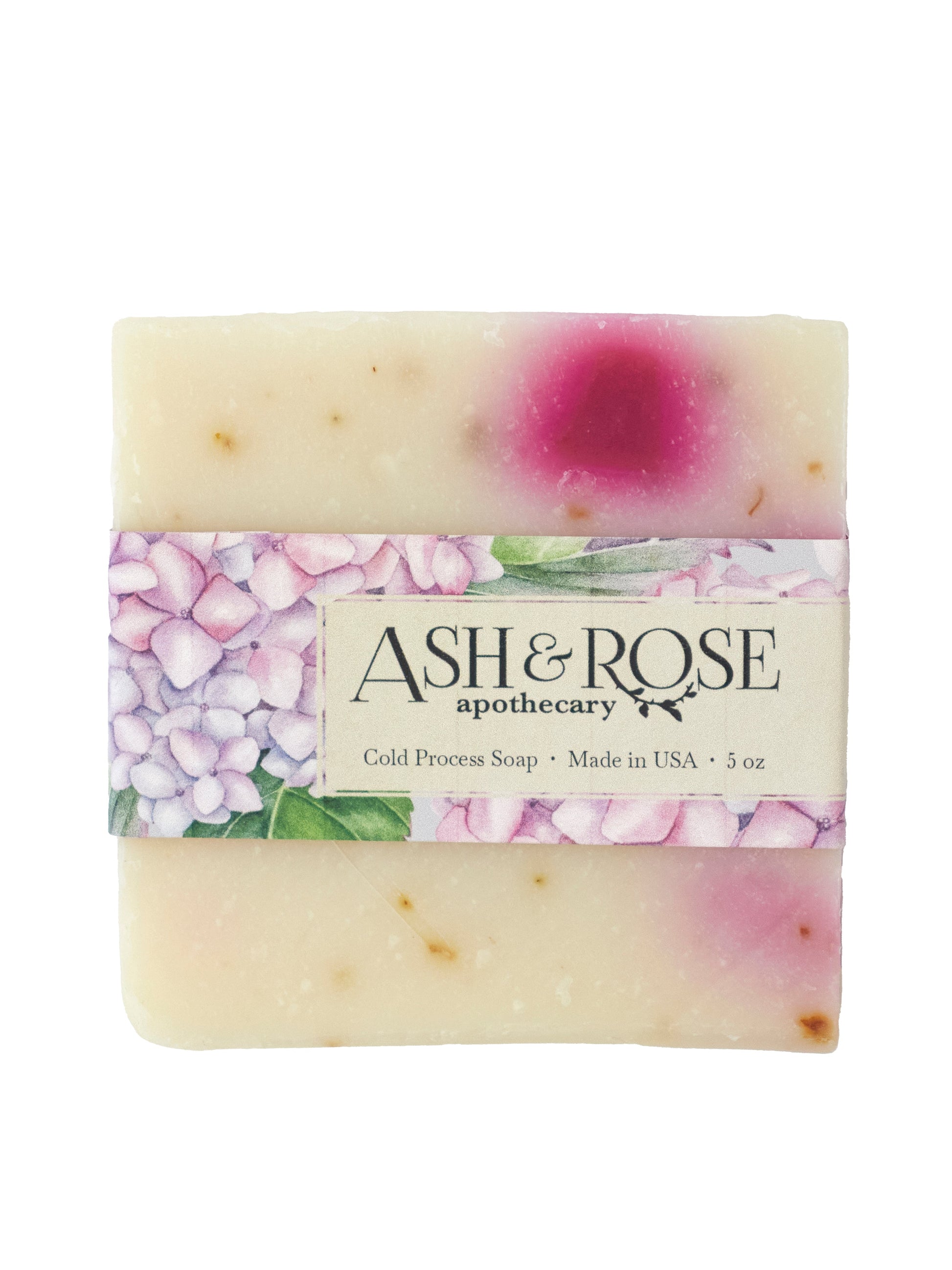 A rectangular Pink Hydrangea Soap Scrub Bar from Ash & Rose features pink and purple spots, wrapped in a floral label reading Ash & Rose, Cold Process Soap, Natural Vegan Soap, Made in USA, 5 oz.
