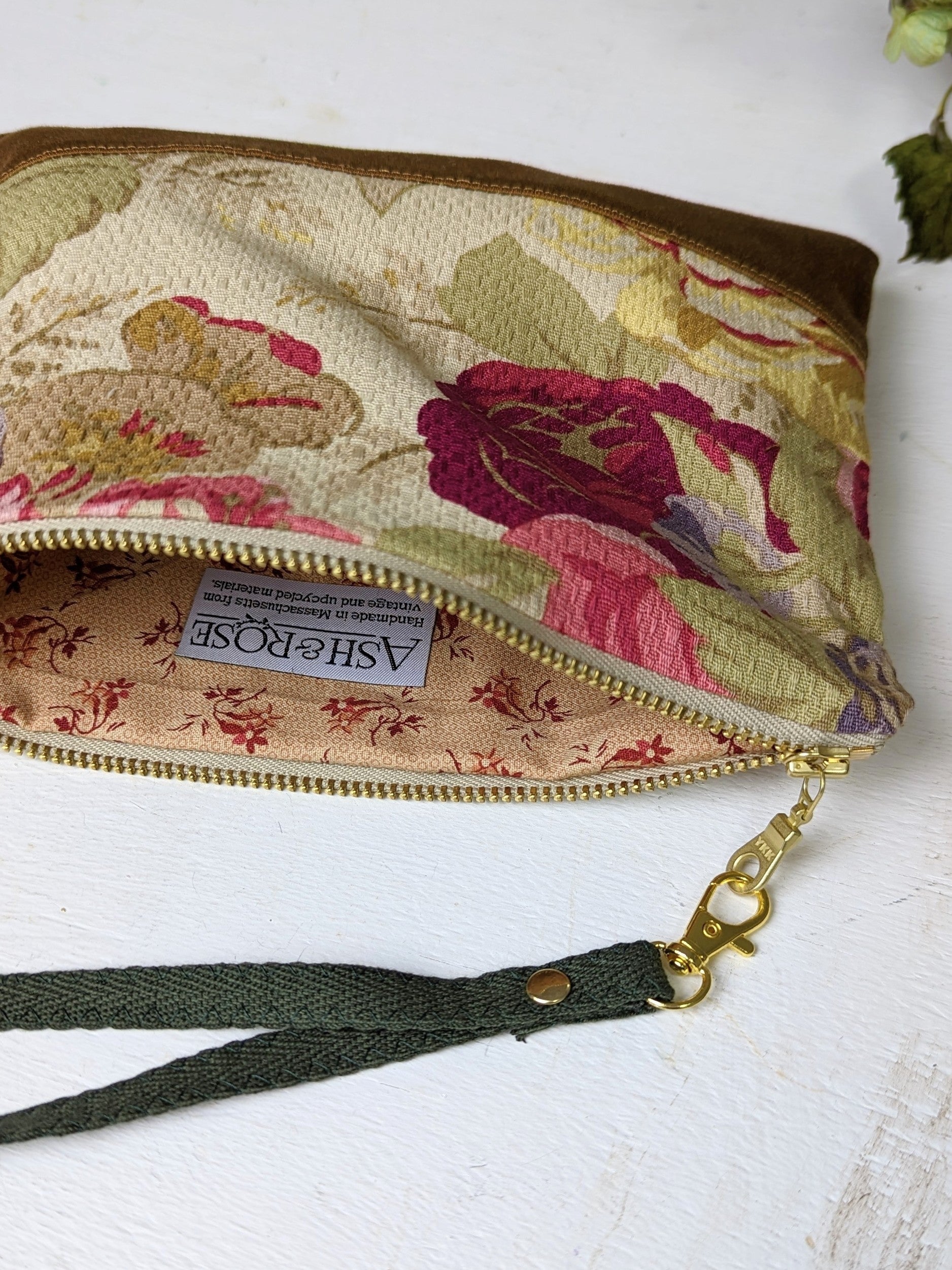 The Antique Roses Purse by Ash & Rose is a handmade wristlet featuring a rose print, gold zipper, dark green strap with metal clasp, and an inner lining with red and beige floral design plus an Ash & Rose label.