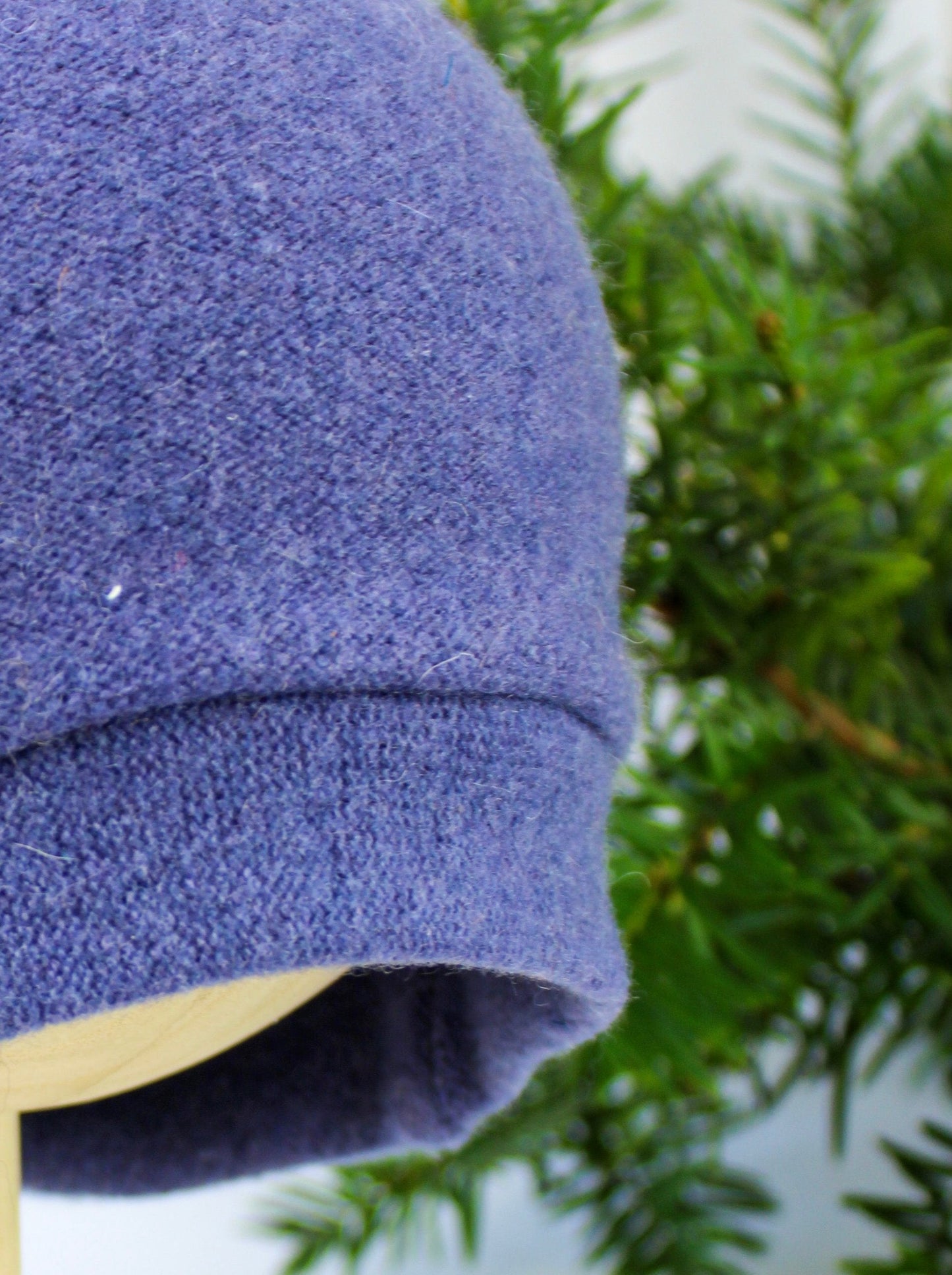 A close-up of the Ash & Rose Sleeping Fox Cashmere Hat - Child in purple, made from recycled cashmere, shown on a mannequin head with green foliage in the background.