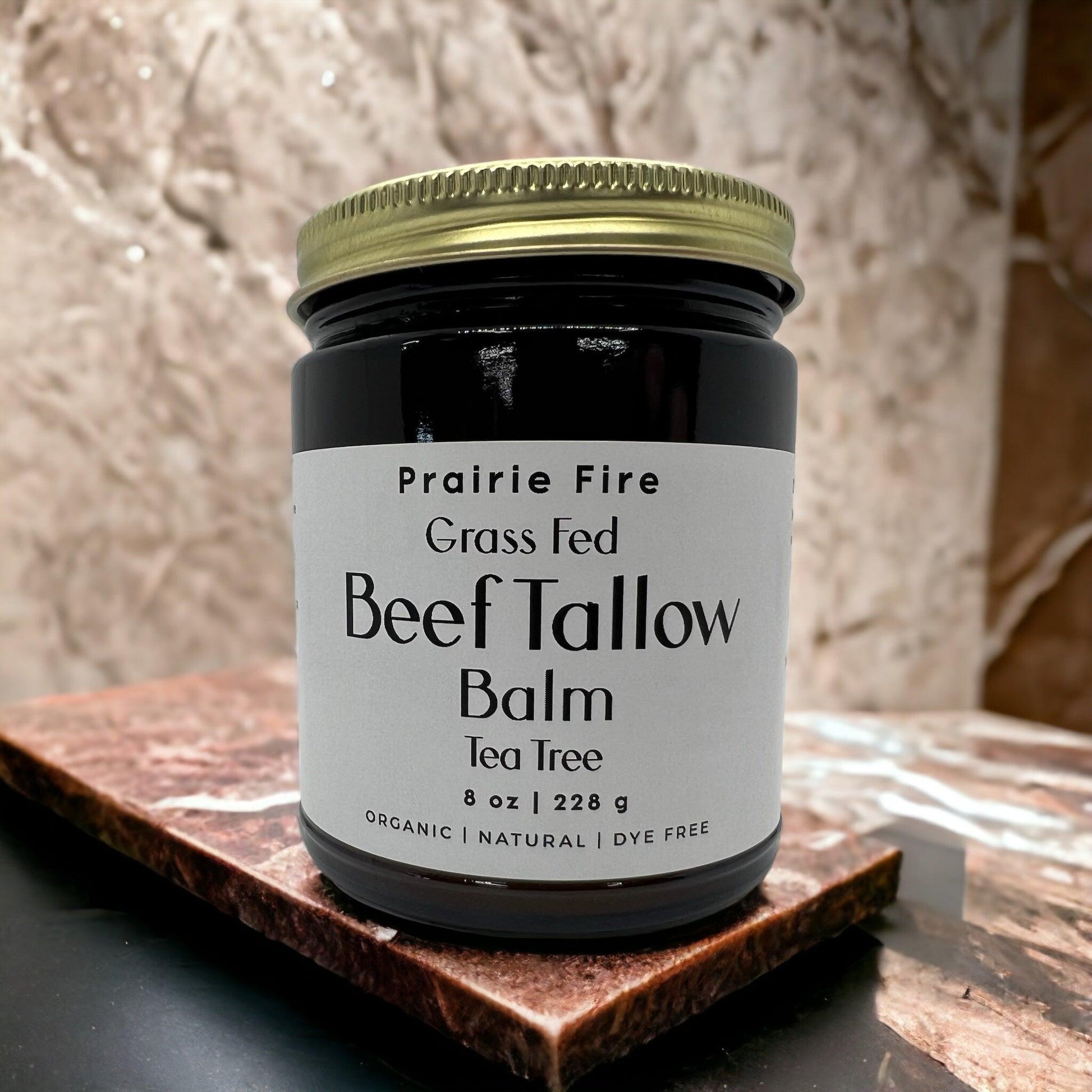 An 8 oz jar of Prairie Fire Tallow, Candles, and Lavender Beef Tallow Balm—organic, grass fed and finished, and made in the USA—rests on a marble surface against a beige backdrop; its a moisturizing natural skin care product.