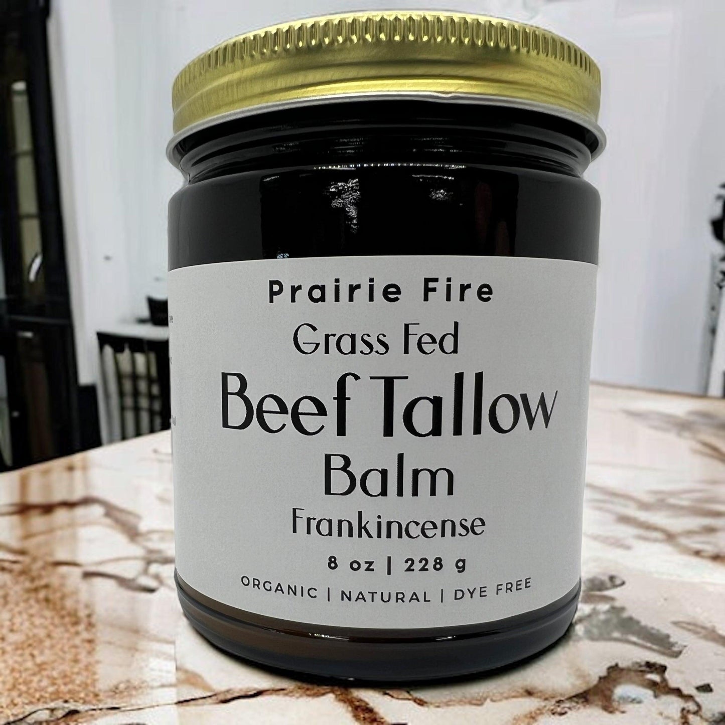 A jar of Prairie Fire Tallow, Candles, and Lavender Beef Tallow Balm—8 oz, organic grass-fed and finished, made in the USA—rests on a marble countertop. This moisturizing skin care comes in a sleek gold-lidded jar with a white label.