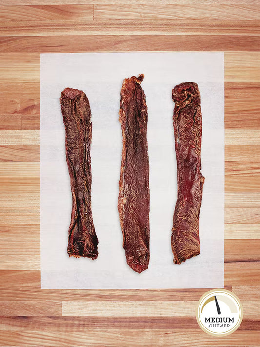 Three Farm Hounds Beef Weasand (esophagus) chews, made from pasture-raised cattle, are lined up on parchment atop a wooden surface. A circular badge in the corner indicates they are for Medium Chewers.