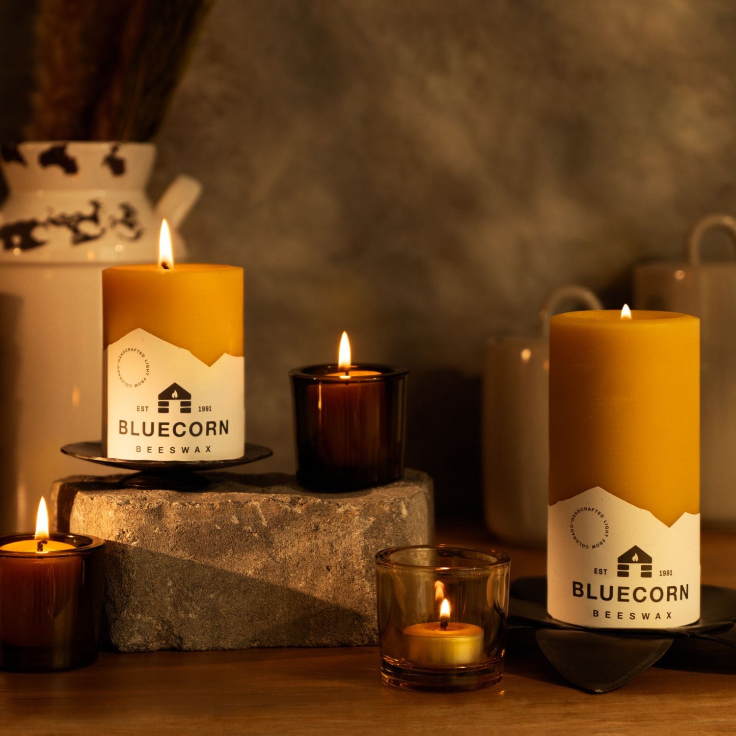 Pure beeswax pillar candles by Bluecorn Candles displayed with votives and tea lights in recycled glass holders.