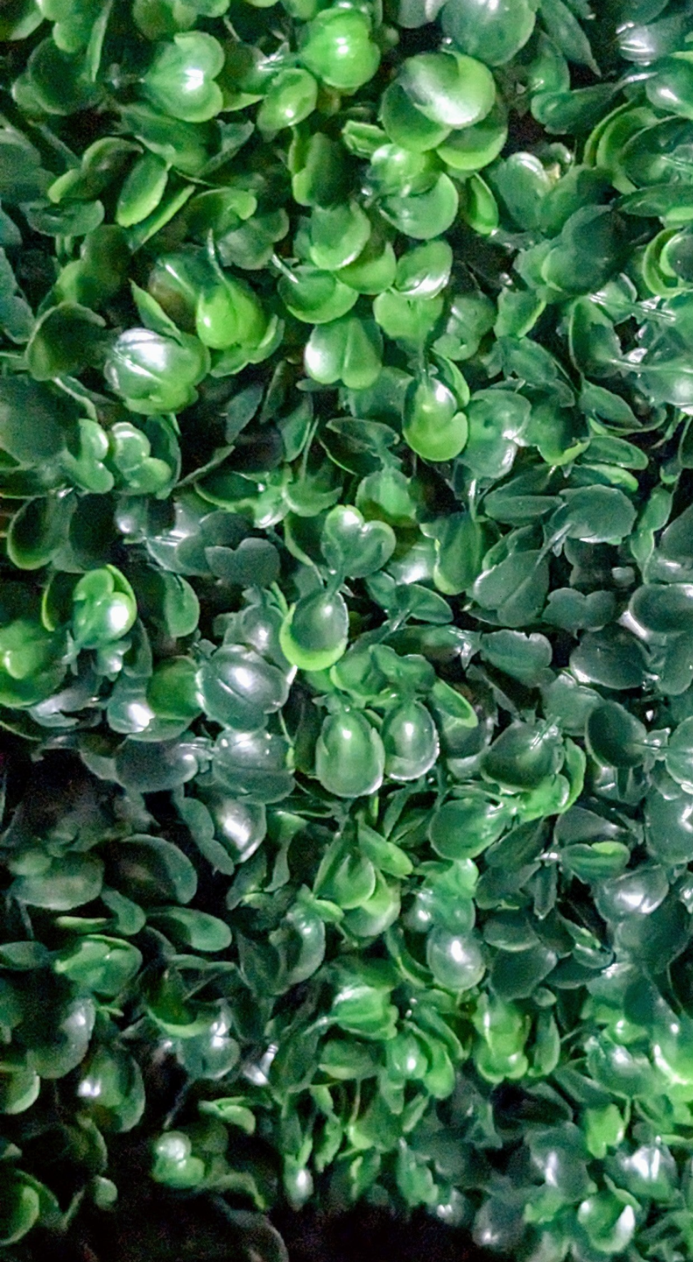 Artificial plant wall lush green leaves showing varied tones and textures of deep emerald and bright green highlights.
