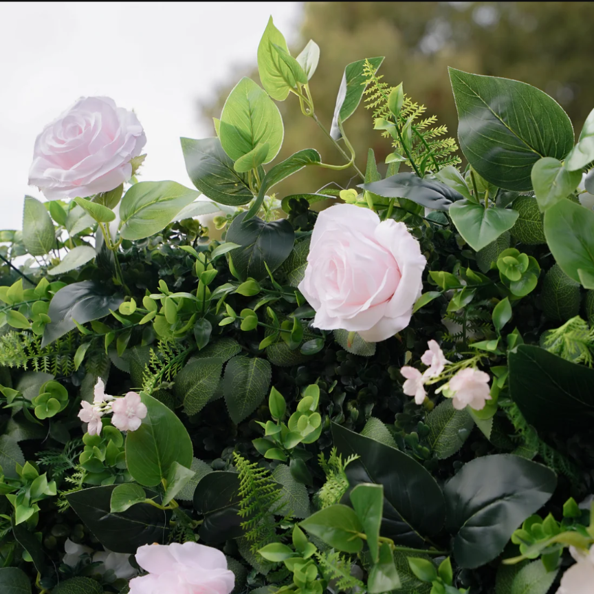 Artificial floral arrangement featuring pale pink roses, delicate light pink accent flowers, and lush green foliage including ferns and eucalyptus-like leaves.
