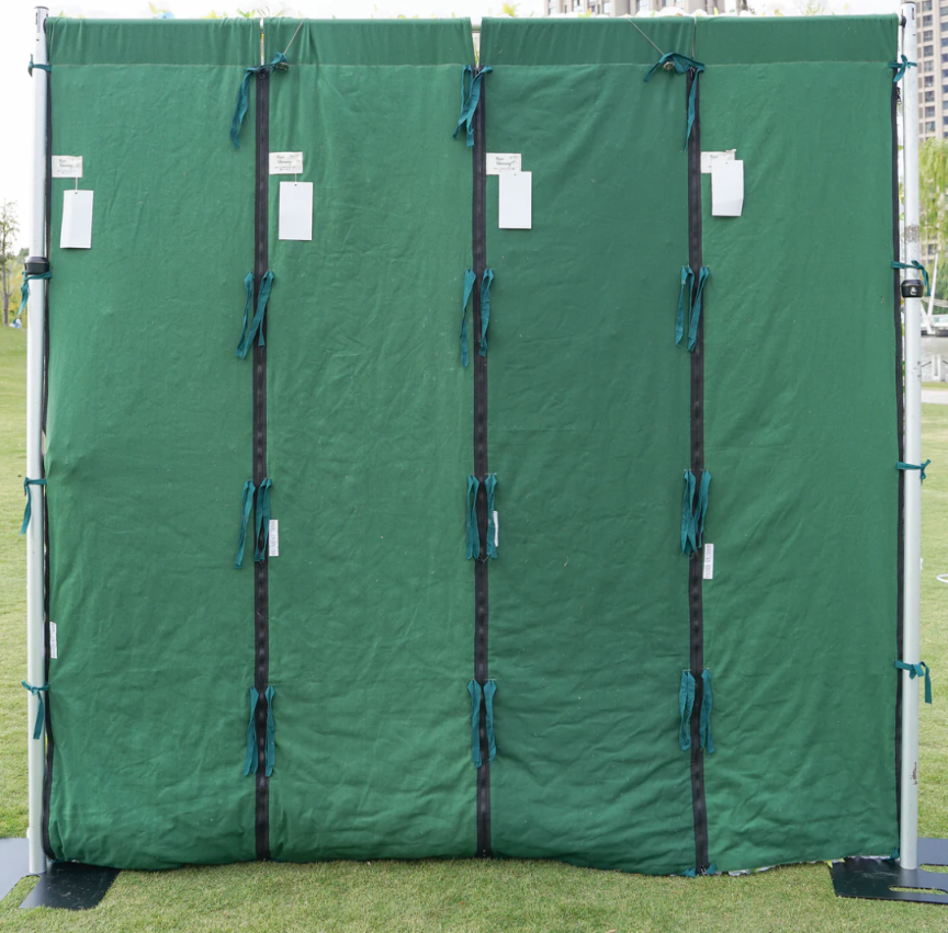Fabric backdrop green panels with black straps and white tags outdoors on grass.