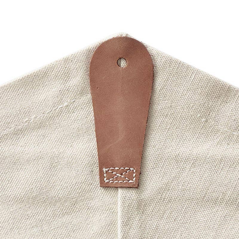 A close-up of the Bouquet Bag - BFF by Blessings Grow Meadows Merch & More, a beige reusable canvas bag with a brown leather tab featuring white stitching and a small hole—perfect for gifting bouquets.