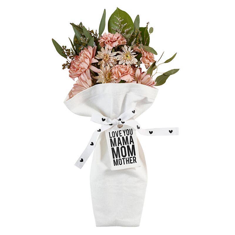 The Bouquet Bag - Mama by Blessings Grow Meadows Merch & More features pink and beige flowers in a reusable bag with a ribbon and tag reading "LOVE YOU MAMA MOM MOTHER" in bold black letters, plus small black heart designs—perfect for mom.