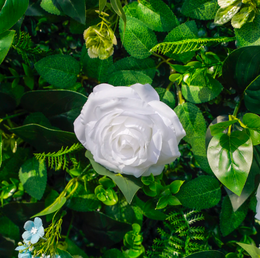 Artificial floral arrangement featuring a large white rose surrounded by vibrant green leaves and small blue flowers
